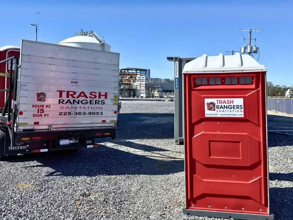 Red Trash Rangers Sanitation portable toilet on a gravel job site next to a Trash Rangers Sanitation service truck