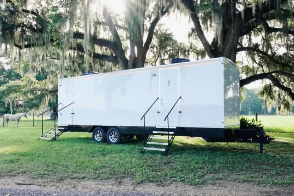White Trash Rangers Sanitation restroom trailer with fold-down steps parked on grass under live oaks draped in Spanish moss