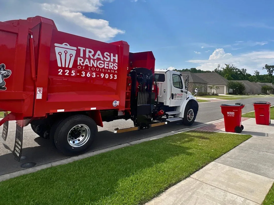 Red Trash Rangers residential garbage truck stopped at the curb beside two red Trash Rangers carts in a Louisiana neighborhood